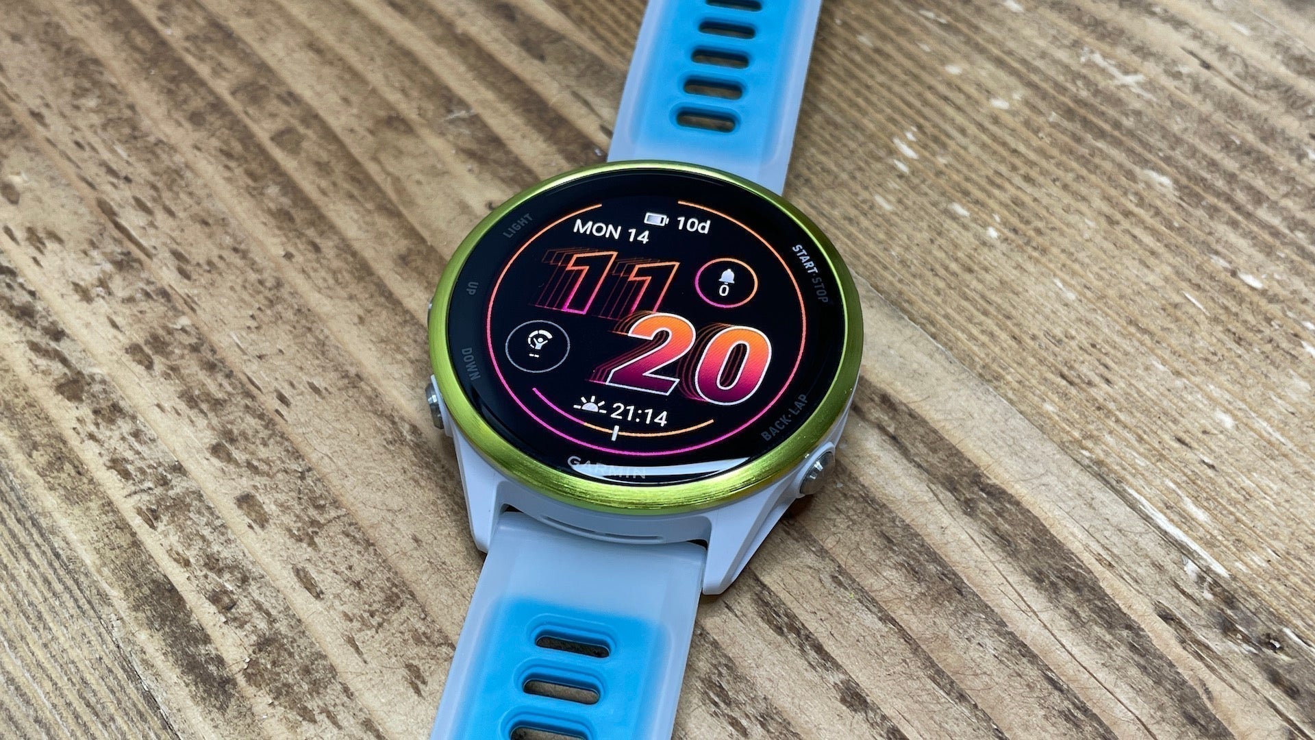The blue and white Garmin Forerunner 570 laying flat on a woodgrain surface