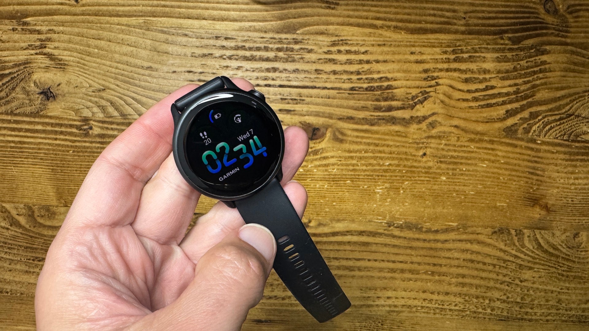 The Garmin vivoactive 6 held in the hand of reviewer and runner Kieran Alger over a wood background