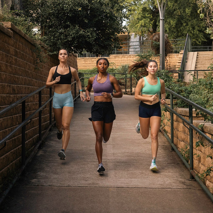 Three women running down a sidewalk next a rock wall and railings with Forerunner 165 running watches on