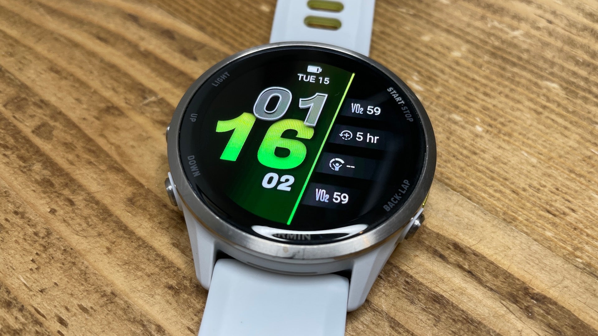 The white Garmin Forerunner 970 running watch laying flat on a woodgrain surface
