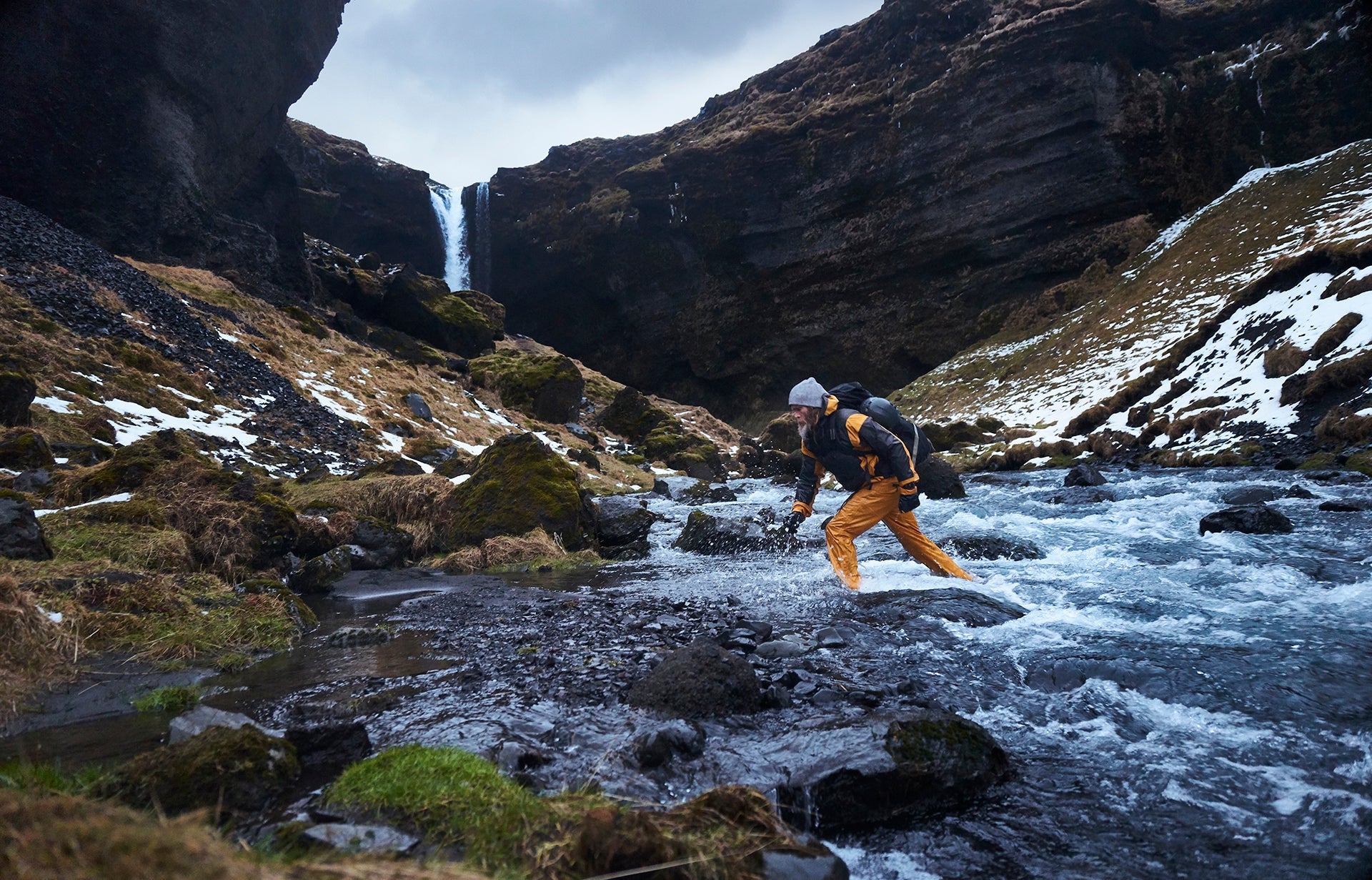 A man wearing a Garmin fenix watch crossing a river in the mountains