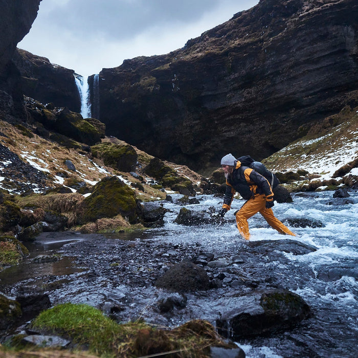 A man wearing a Garmin fenix watch crossing a river in the mountains