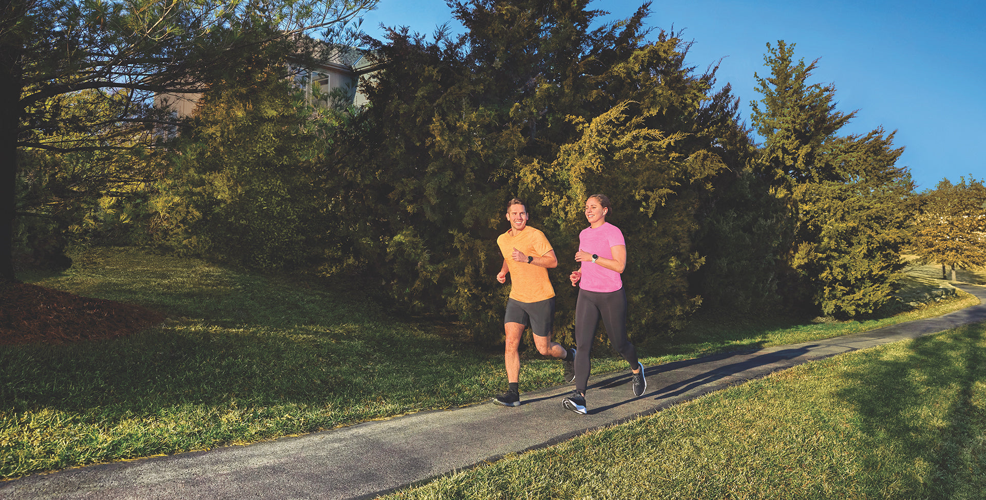 A man and woman running on an asphalt trail wearing Garmin running watches