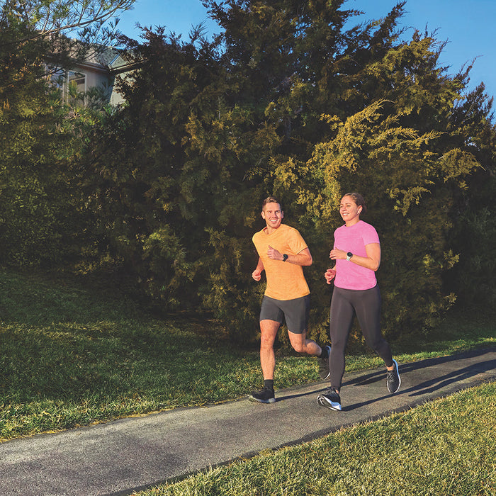 A man and woman running on an asphalt trail wearing Garmin running watches