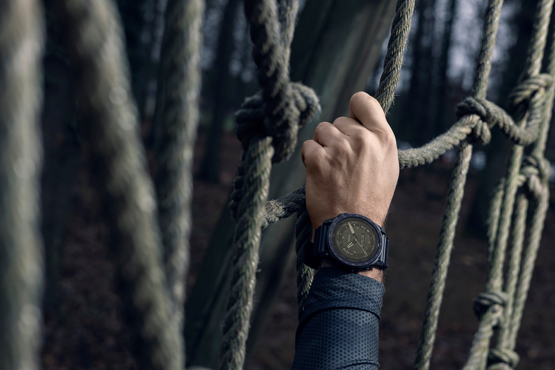 A Garmin tactix 7 AMOLED tactical watch on the wrist of a hand climbing up a rope wall