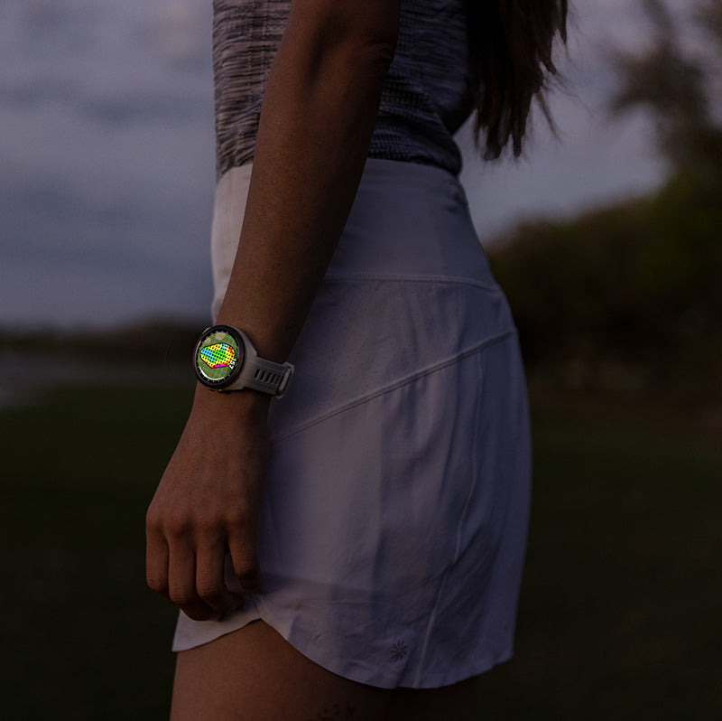 Female golfer wearing a 42 mm Garmin Approach S70 golf watch glowing on her wrist at her side on a golf course at dusk