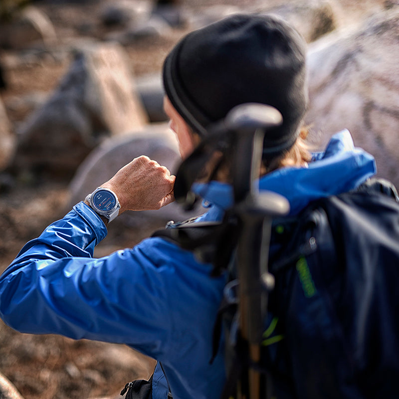 A backpacker pausing on a rocky trail to look at his Garmin fenix 7X outdoor GPS watch