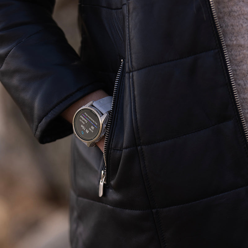 A closeup of a coat pocket with a hand in it with a Garmin fenis 7 sport watch on the wrist