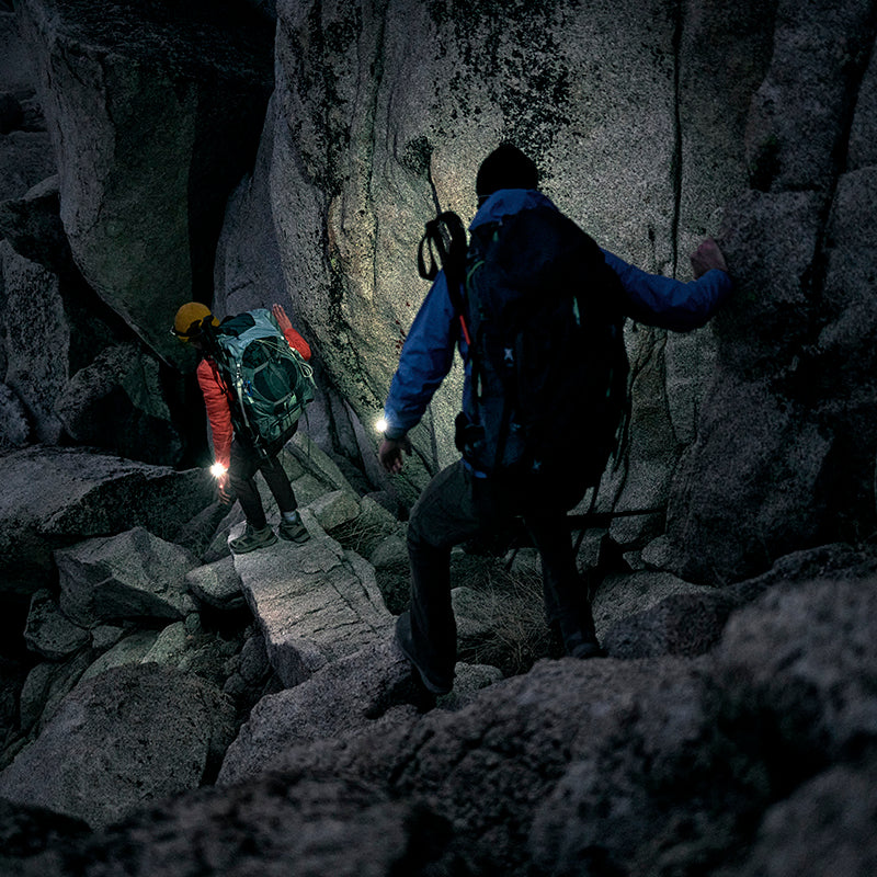 Two backpackers descending a rocky trail with their Garmin fenix 7 watch flashlights shining